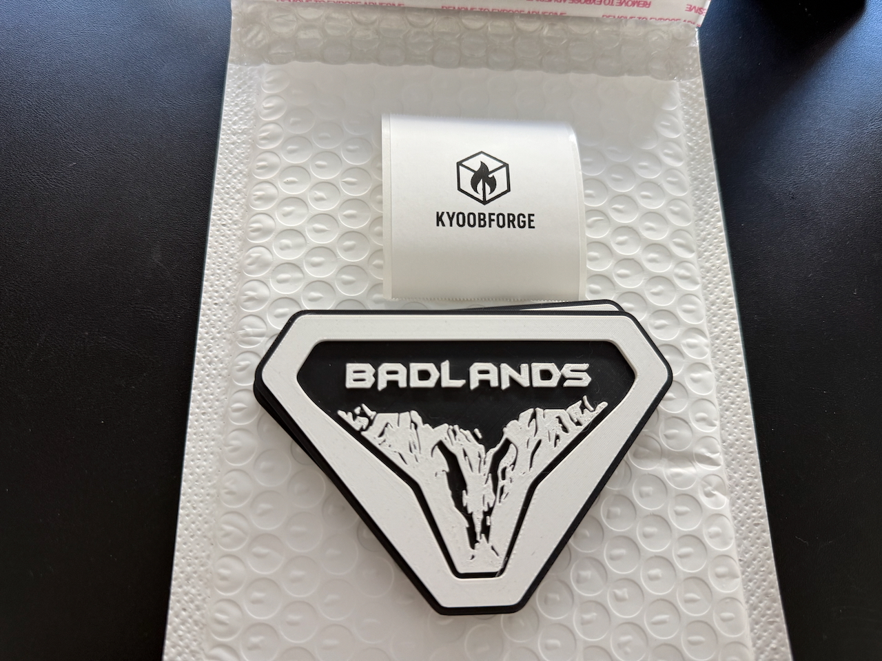 Black and white Badlands badge packaged with KyoobForge label